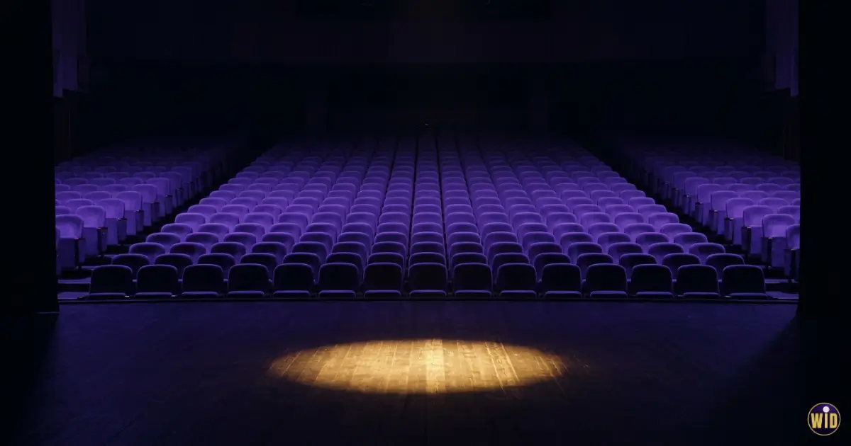 An empty auditorium seen from the stage with a gold spotlight on the floor, evoking dreaming of being naked in public